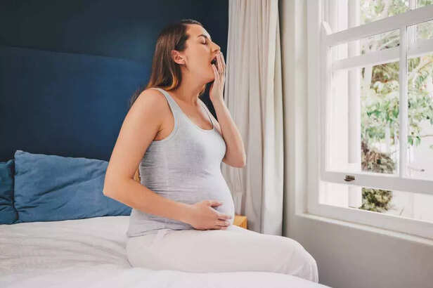 Pregnant woman yawning while sitting on her bed