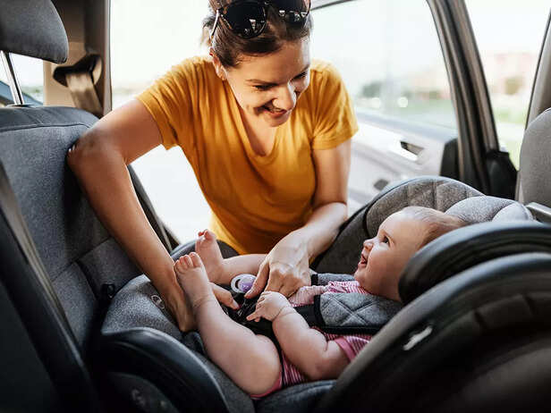 Mother putting baby girl in baby car seat