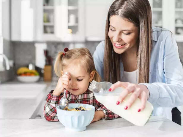 CHILD PREPARING CEREAL WITH MOTHER'S HELP