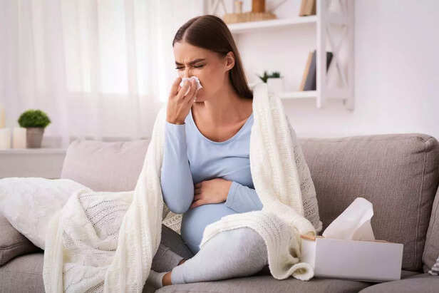 Pregnant woman blowing nose in tissue sitting on sofa indoor
