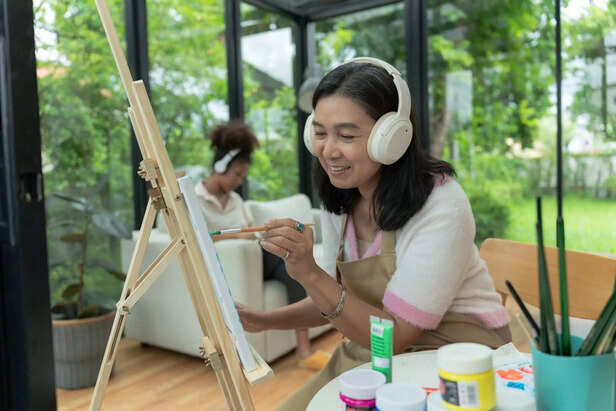 Pleasant Asian female mother in apron with palette and brush painting