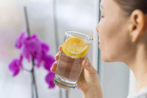 Woman drinking summer refreshing fruit flavored infused water with fresh organic lemon.