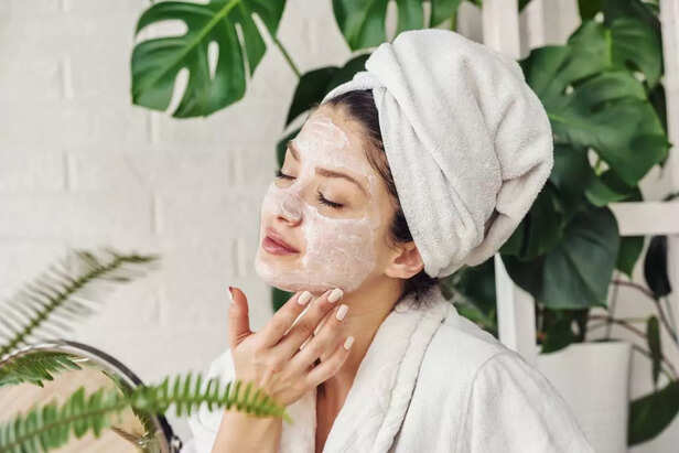 Young woman cleaning face with natural cosmetics. How to get clear and glowing skin. Portrait of young woman with clay face mask on wearing bathrobe. Homemade Face Mask