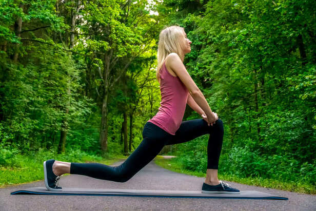 young blonde woman does a leg lunge exercise in the woods on a summer day