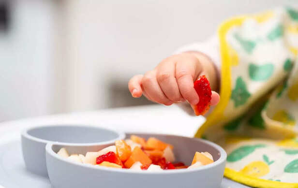 Baby Hand with a Piece of Fruits Sitting in Child's Chair Kid Eating Healthy Food