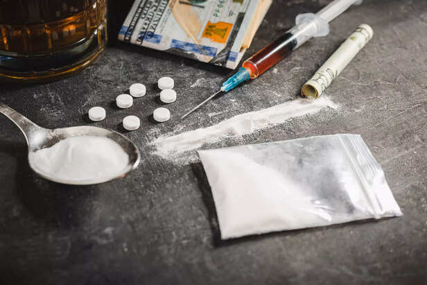 Drugs white pill, syringe with a dose of narcotic substances, white powder cocaine, alcohol drink in a glass and US dollar currency on dark background. Concept of addiction, abuse and bad habits