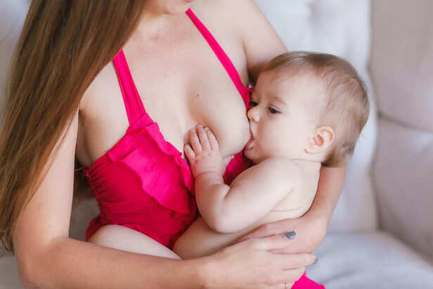 Young woman breastfeeding her little baby at home, closeup. Wearing pink dress.