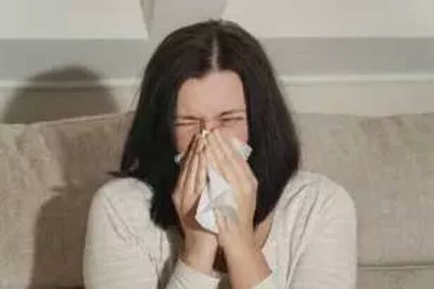 Middle aged mature woman suffering from allergy rhinitis at home. Symptoms of cold or allergy. Woman sneezes in white tissue.