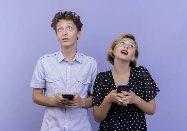 couple-standing-holding-smartphones-looking-confused
