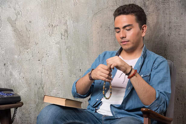 young-man-putting-bracelet-sitting-chair-with-book