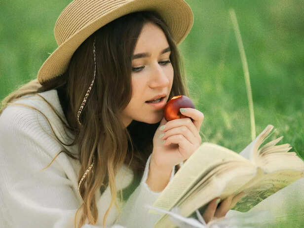A woman eating a peach while reading
