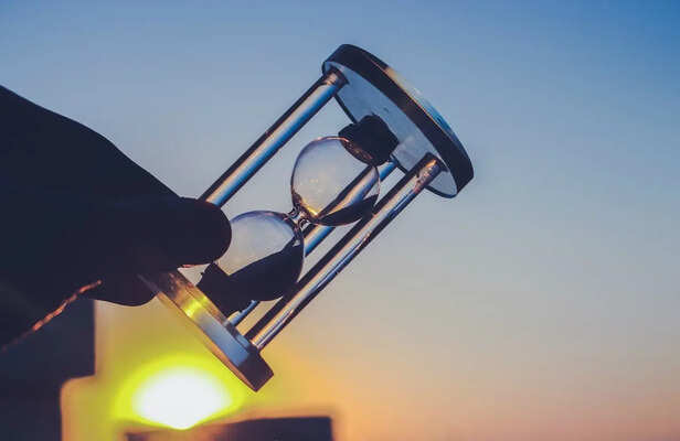 Hourglass held against a vibrant sunset