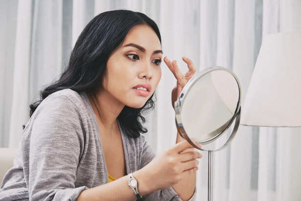 Woman noticing dull skin in mirror