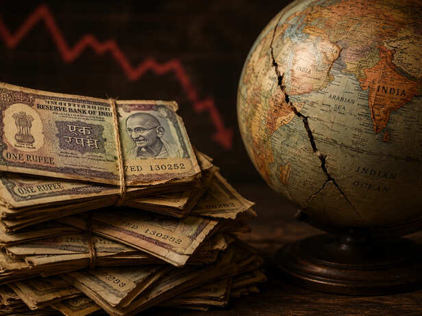 A stack of old Indian rupee notes beside a globe, symbolising a nation running out of foreign currency.