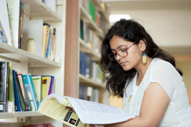 Portrait of a smiling young Indian student reading a book in a library ·  Free Stock Photo